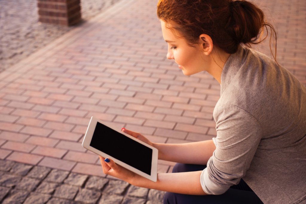 Person sitting on stoop reading something on a tablet.