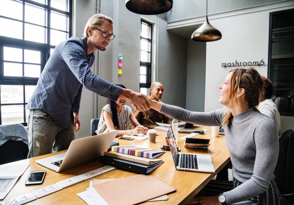 person standing and shaking the hand of other person sitting at a conference room table.